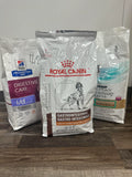 Three bags of Royal Canin veterinary diet products on a wooden surface.