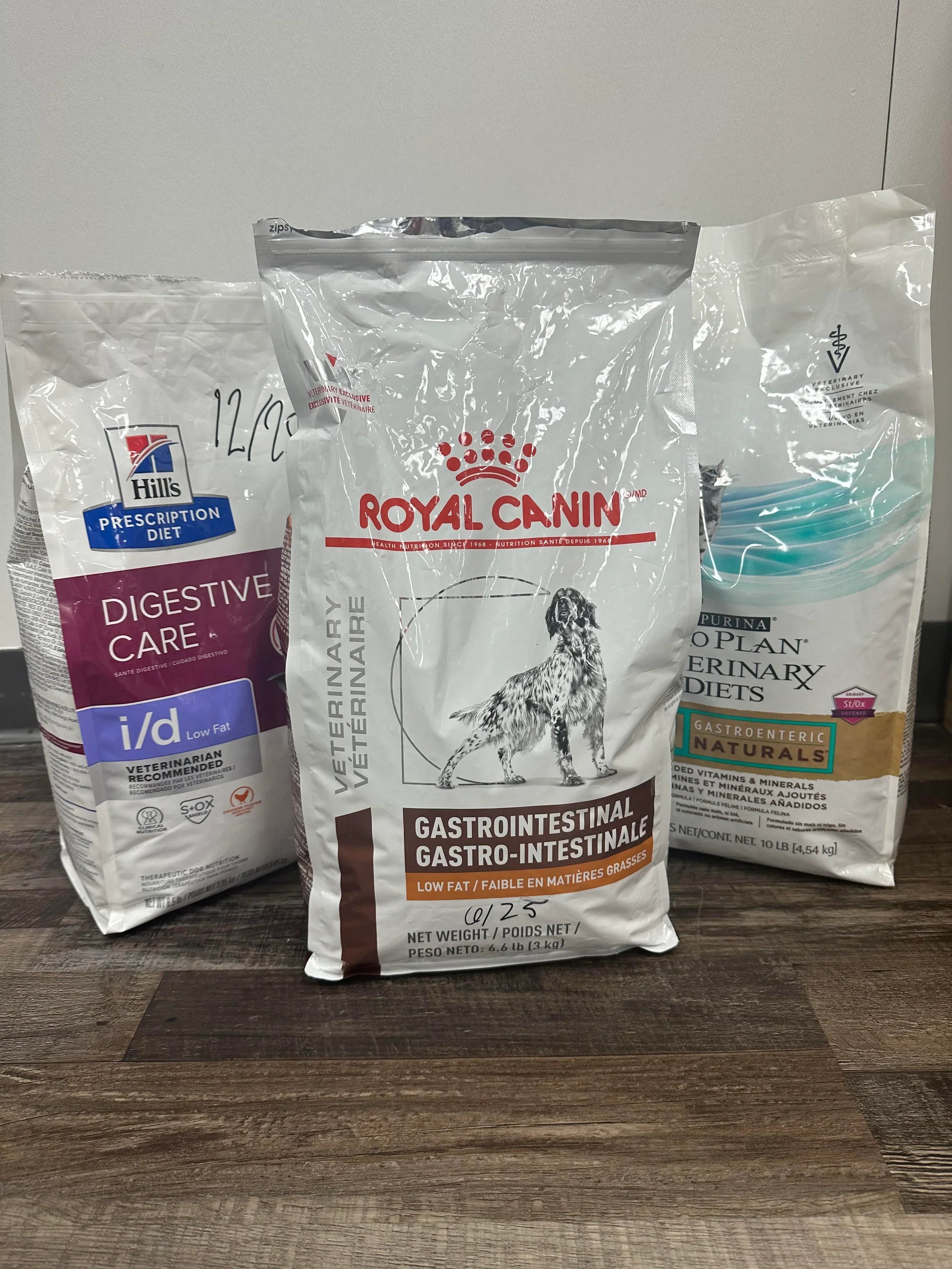 Three bags of Royal Canin veterinary diet products on a wooden surface.